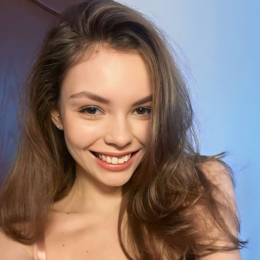 Een close-up van OnlyFans-model Emilycutee met lang, golvend bruin haar, die warm naar de camera glimlacht tegen een zacht verlichte achtergrond.